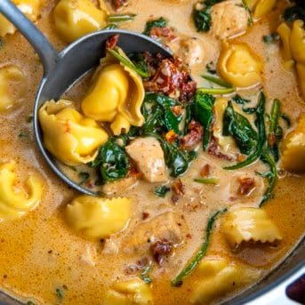 Ladle of Tuscan Chicken Tortellini Soup held in the pot.