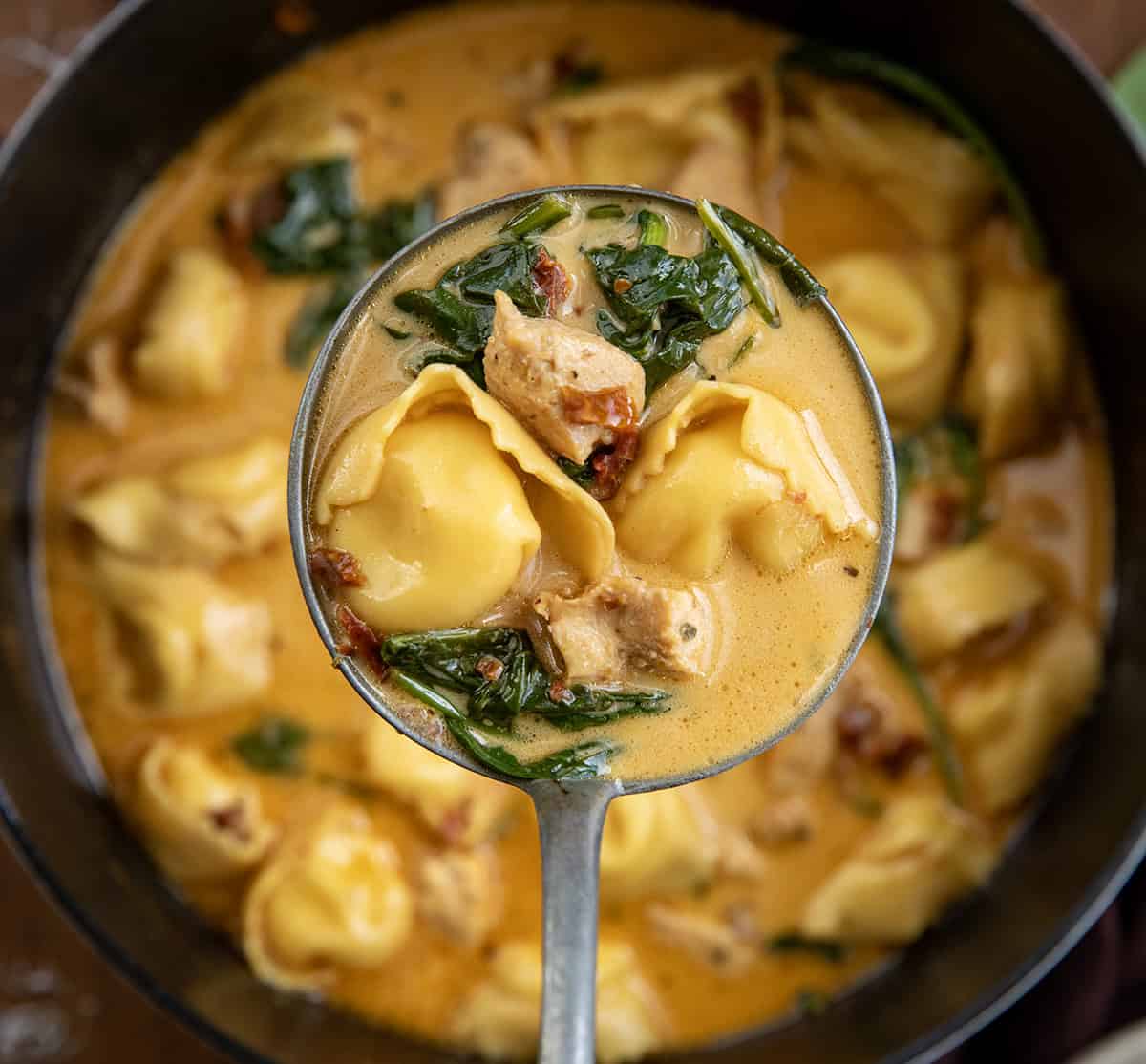 Ladle of Tuscan Chicken Tortellini Soup held above the pot.