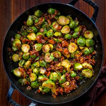Skillet of Bacon Jam Brussels Sprouts on a wooden table from overhead.