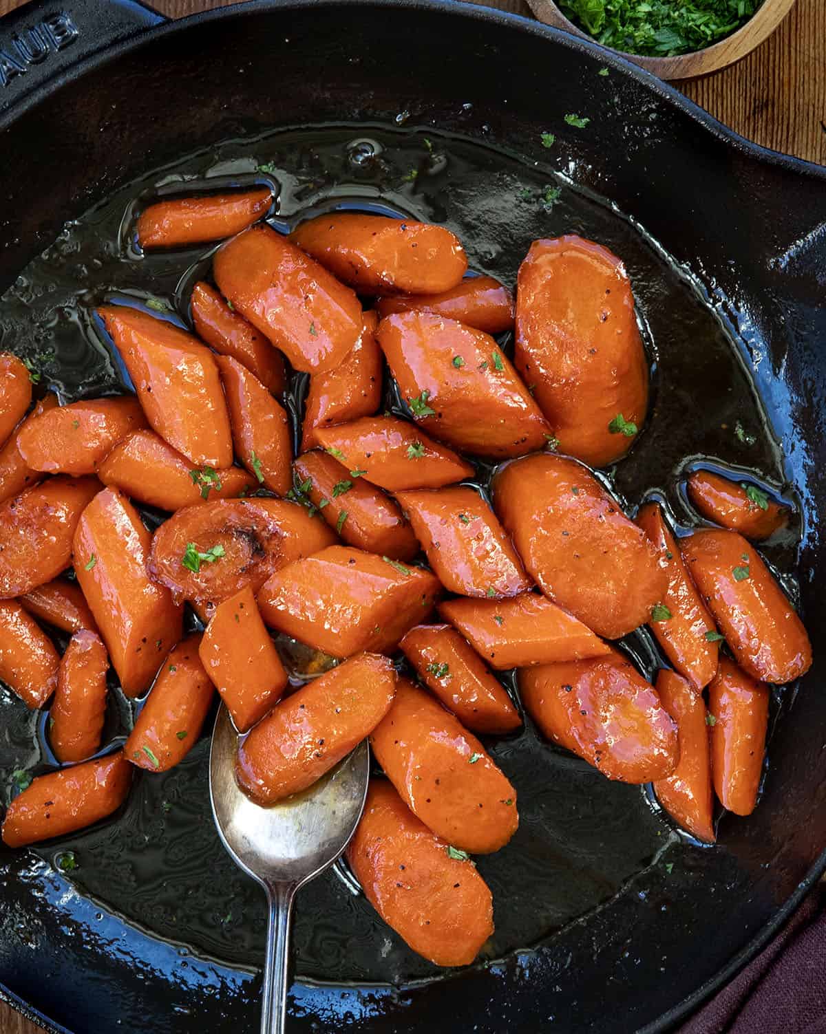 Elevate your holiday table or any weeknight dinner with Candied Carrots, sweet and buttery glazed carrots perfect for any occasion! Skillet of Candied Carrots with a spoon resting in the pan from overhead.
