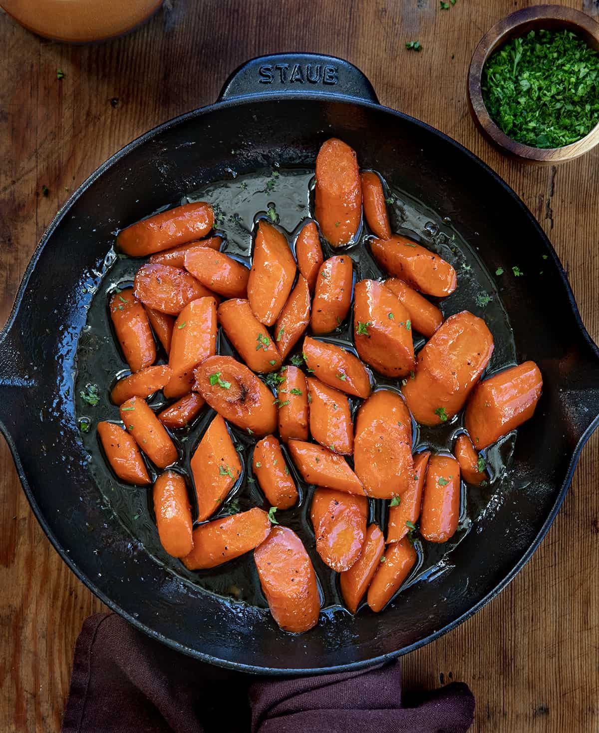 Elevate your holiday table or any weeknight dinner with Candied Carrots, sweet and buttery glazed carrots perfect for any occasion! Skillet of Candied Carrots on a wooden table from overhead.