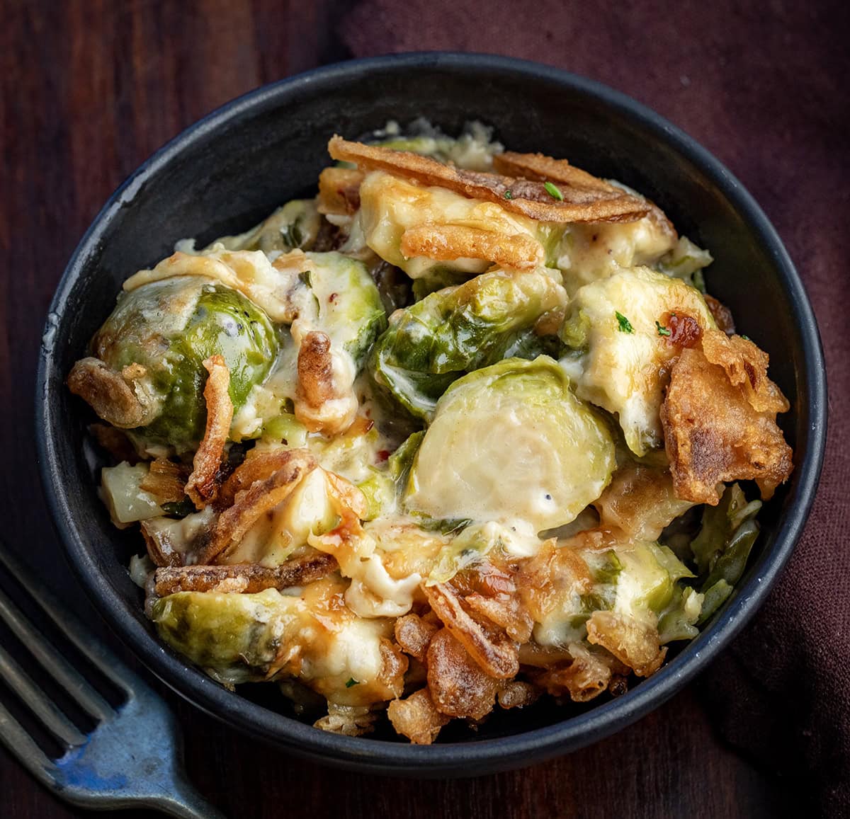 This Cheesy Brussels Sprout Casserole takes tender Brussels sprouts and coats them in a rich, creamy cheese sauce before baking them under a layer of golden, crispy onions. It’s warm, comforting, and indulgent in the best way... an easy side dish that turns a simple vegetable into something everyone will want seconds of! Bowl of Cheesy Brussels Sprout Casserole.