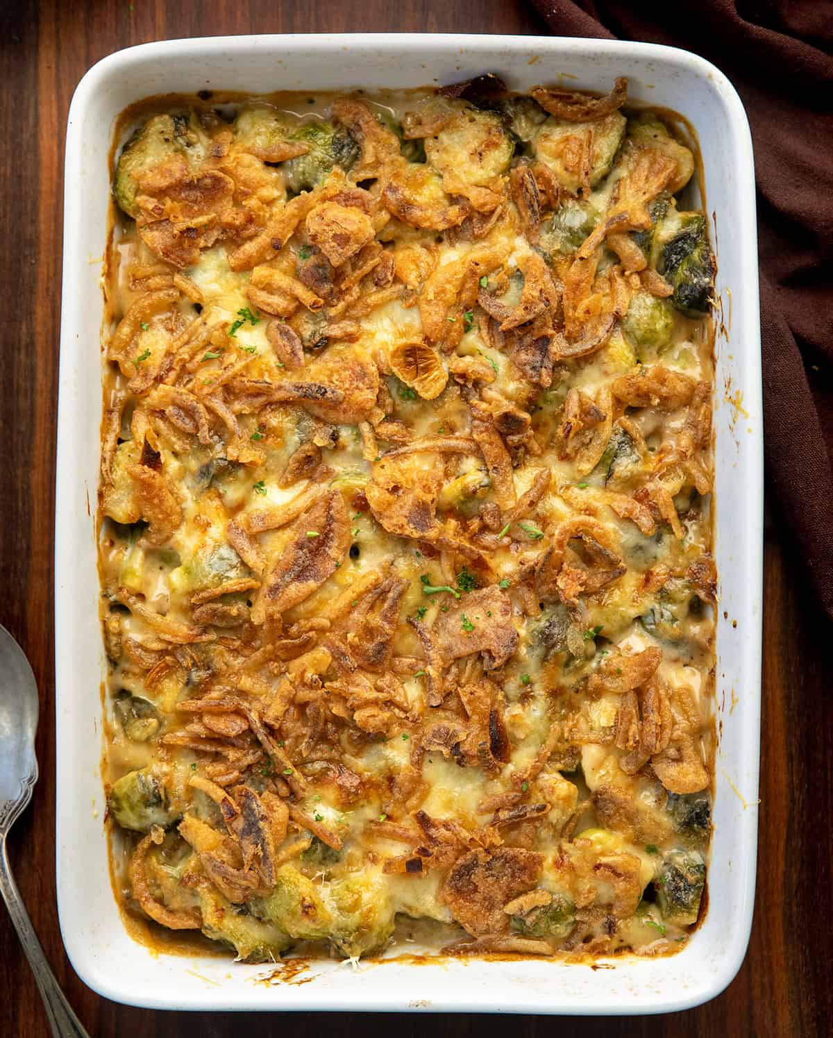 This Cheesy Brussels Sprout Casserole takes tender Brussels sprouts and coats them in a rich, creamy cheese sauce before baking them under a layer of golden, crispy onions. It’s warm, comforting, and indulgent in the best way... an easy side dish that turns a simple vegetable into something everyone will want seconds of! Pan of Cheesy Brussels Sprout Casserole on a wooden table.