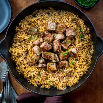 Skillet of Steak and Caramelized Onion Orzo on a wooden table from overhead.