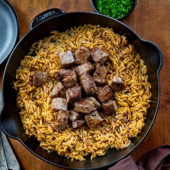Skillet of Steak and Caramelized Onion Orzo on a wooden table from overhead.