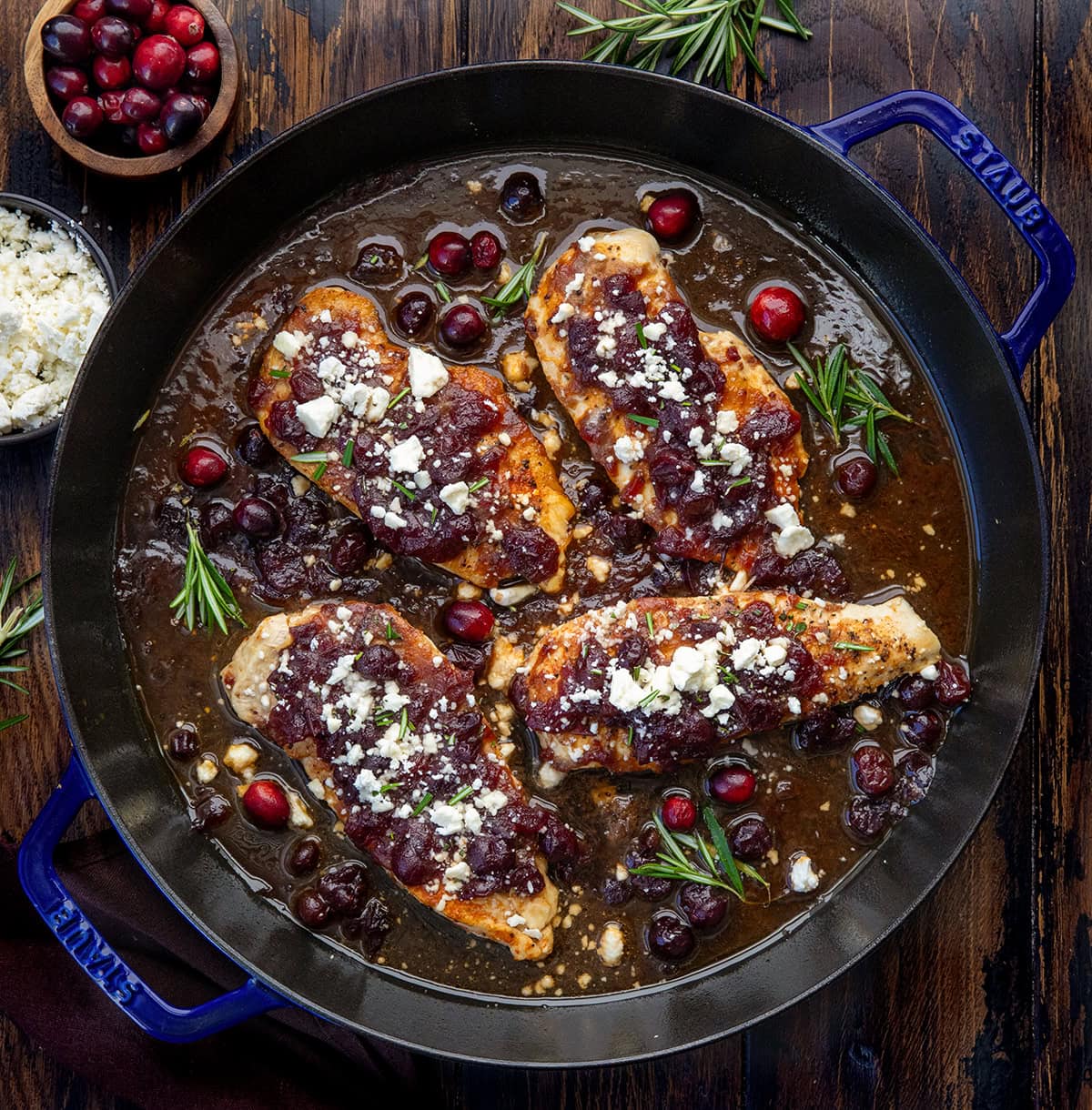 Sweet, tangy, and full of flavor, this Cranberry Feta Chicken Bake is a simple one-pan meal that looks as beautiful as it tastes! It’s perfect for a weeknight dinner and done in under 30 minutes! Skillet of Cranberry Feta Chicken Bake on a wooden table from overhead.