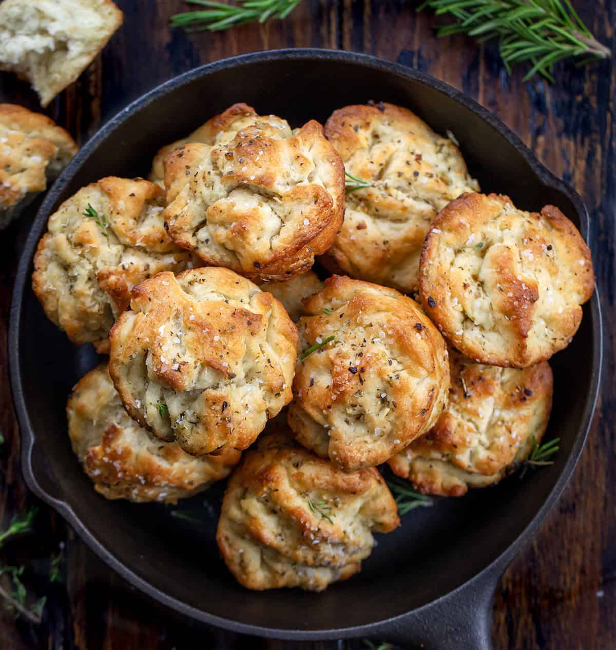 These Focaccia Muffins are crispy on the outside, soft and airy inside, and bursting with garlic, olive oil, and herbs. Focaccia Muffins in a small black skillet on a wooden table from overhead.
