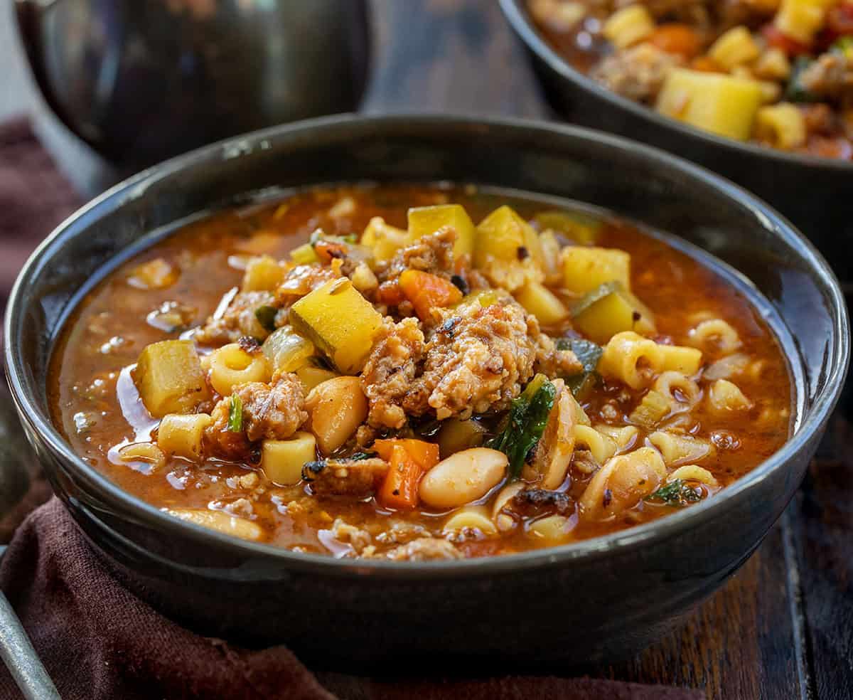 Enjoy a warm bowl of Minestrone Soup with Sausage, packed with vegetables and flavors for a cozy meal in under an hour! Bowl of Minestrone Soup with Sausage on a wooden table close up.