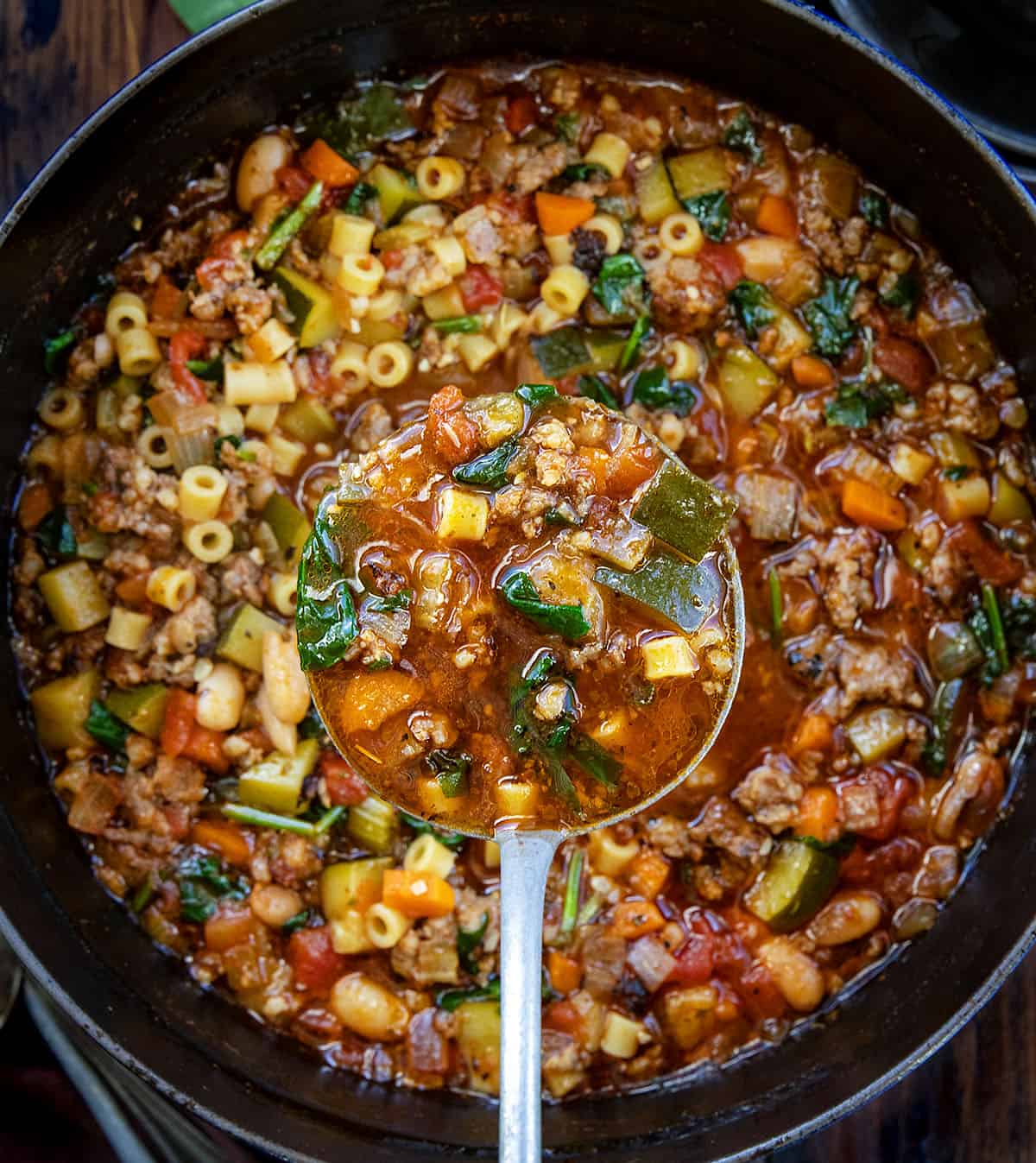 Enjoy a warm bowl of Minestrone Soup with Sausage, packed with vegetables and flavors for a cozy meal in under an hour! Ladle full of Minestrone Soup with Sausage being held above the pot.