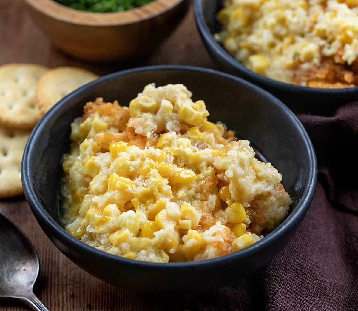 Cozy, creamy, and crowned with a buttery cracker topping, this Scalloped Corn is the kind of classic holiday side that always disappears fast! Bowls of Scalloped Corn on a wooden table close up.