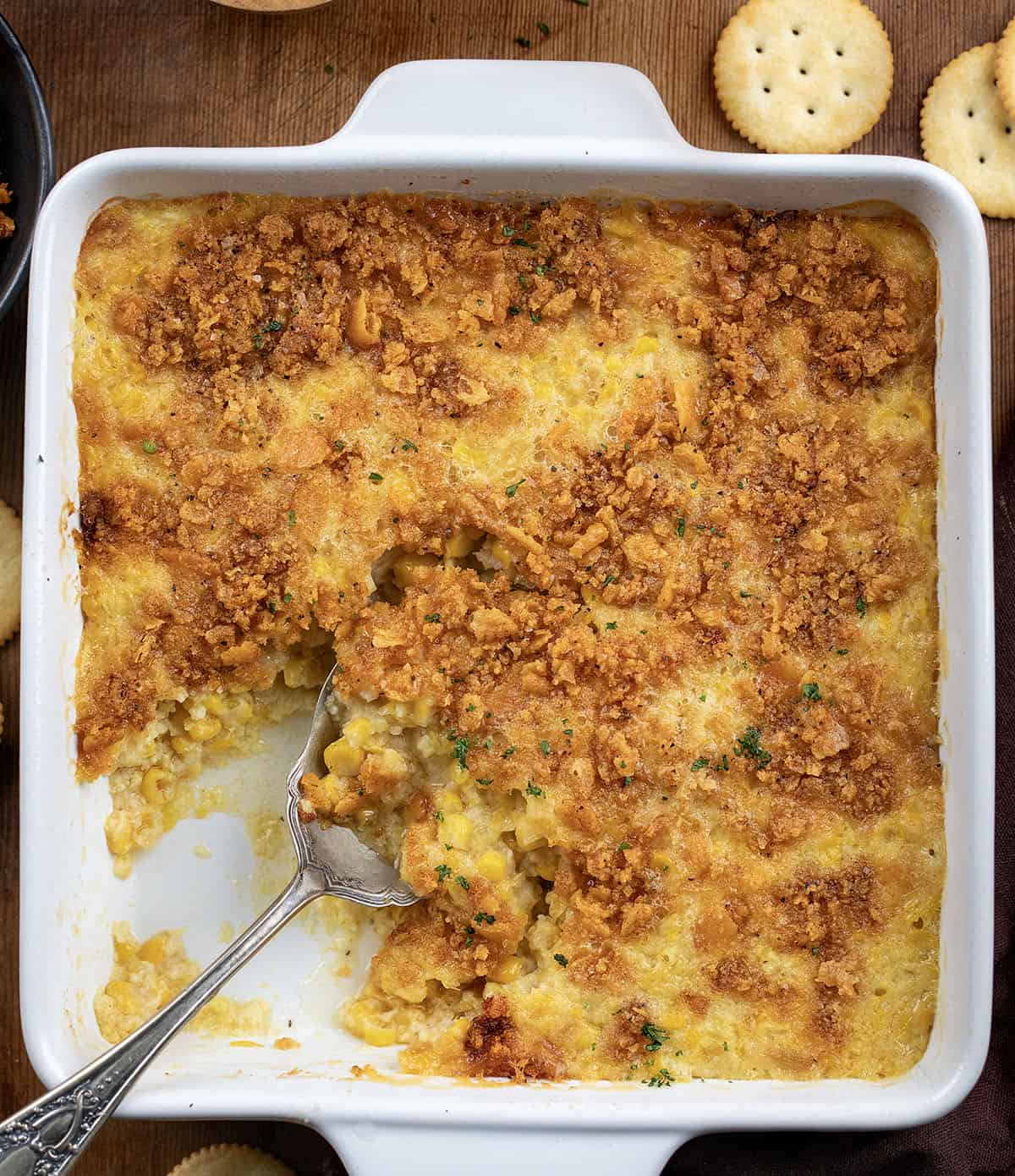 Cozy, creamy, and crowned with a buttery cracker topping, this Scalloped Corn is the kind of classic holiday side that always disappears fast! Dish filled with Scalloped Corn and a spoon in the dish.