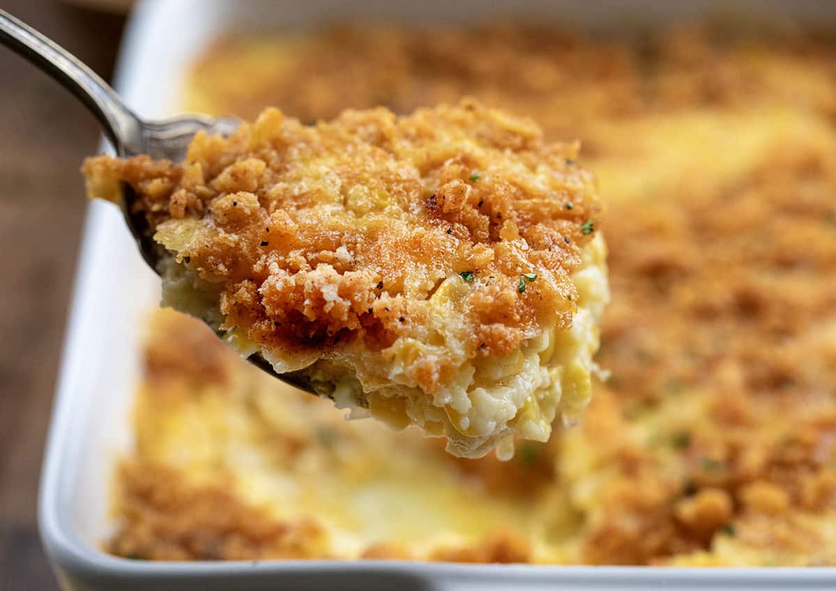 Cozy, creamy, and crowned with a buttery cracker topping, this Scalloped Corn is the kind of classic holiday side that always disappears fast! Spoonful of Scalloped Corn being held above the dish.