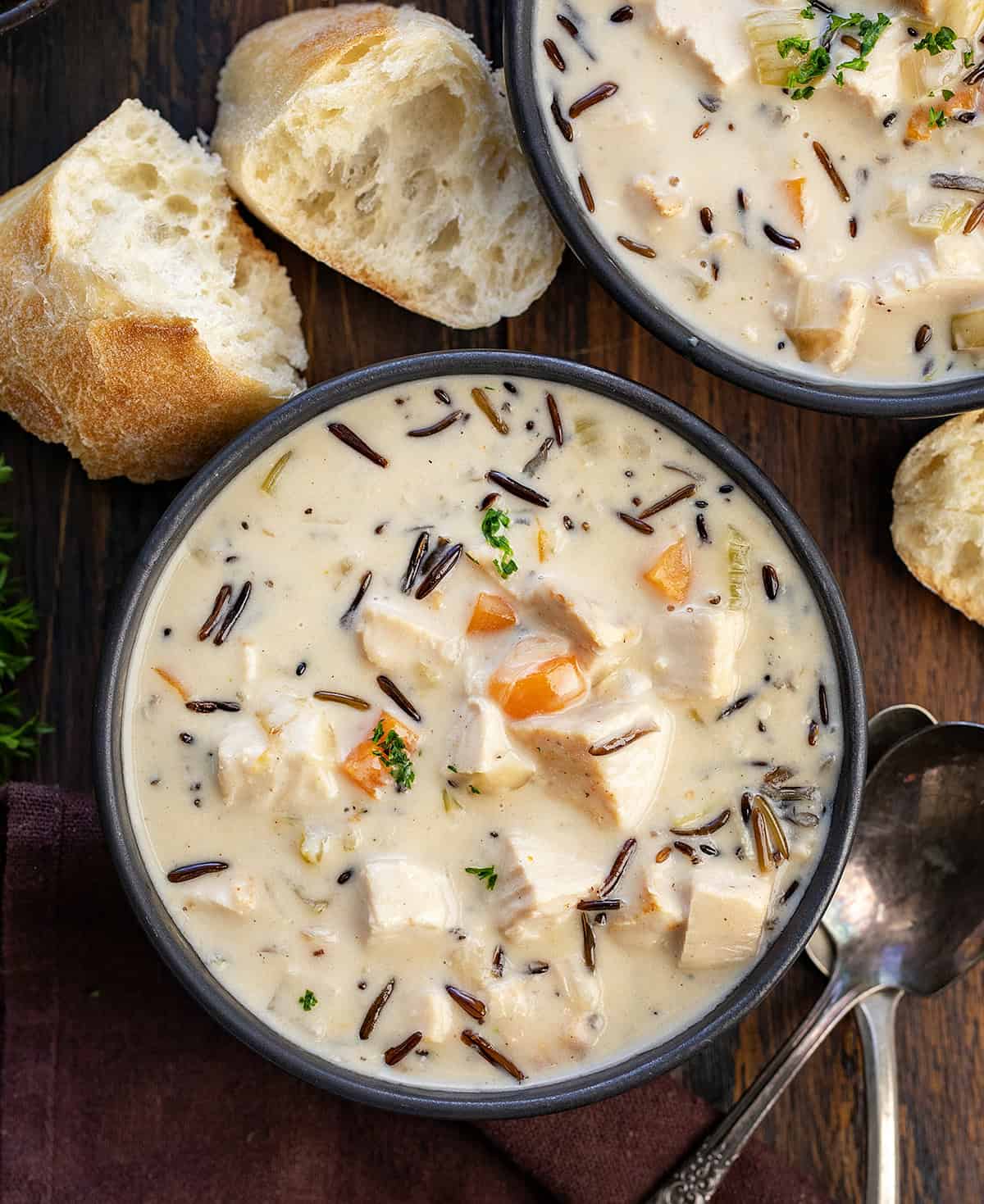 Black bowls of Turkey Wild Rice Soup on wooden table from overhead.