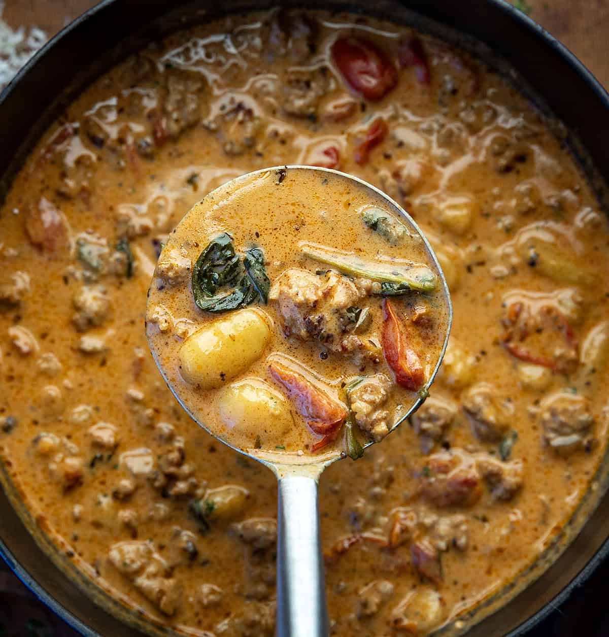 Pot of Tuscan Sausage Gnocchi Soup with a ladle held above it full of soup.