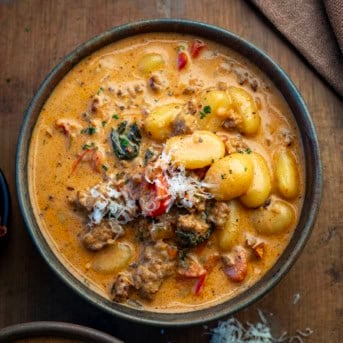 Bowl of Tuscan Sausage Gnocchi Soup on a wooden table.