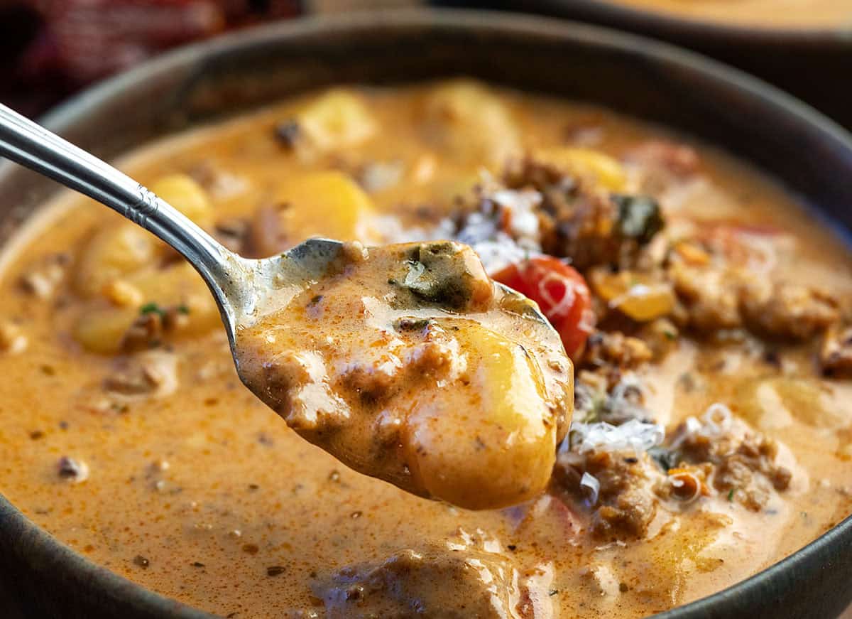 Spoonful of Tuscan Sausage Gnocchi Soup being held above the bowl.