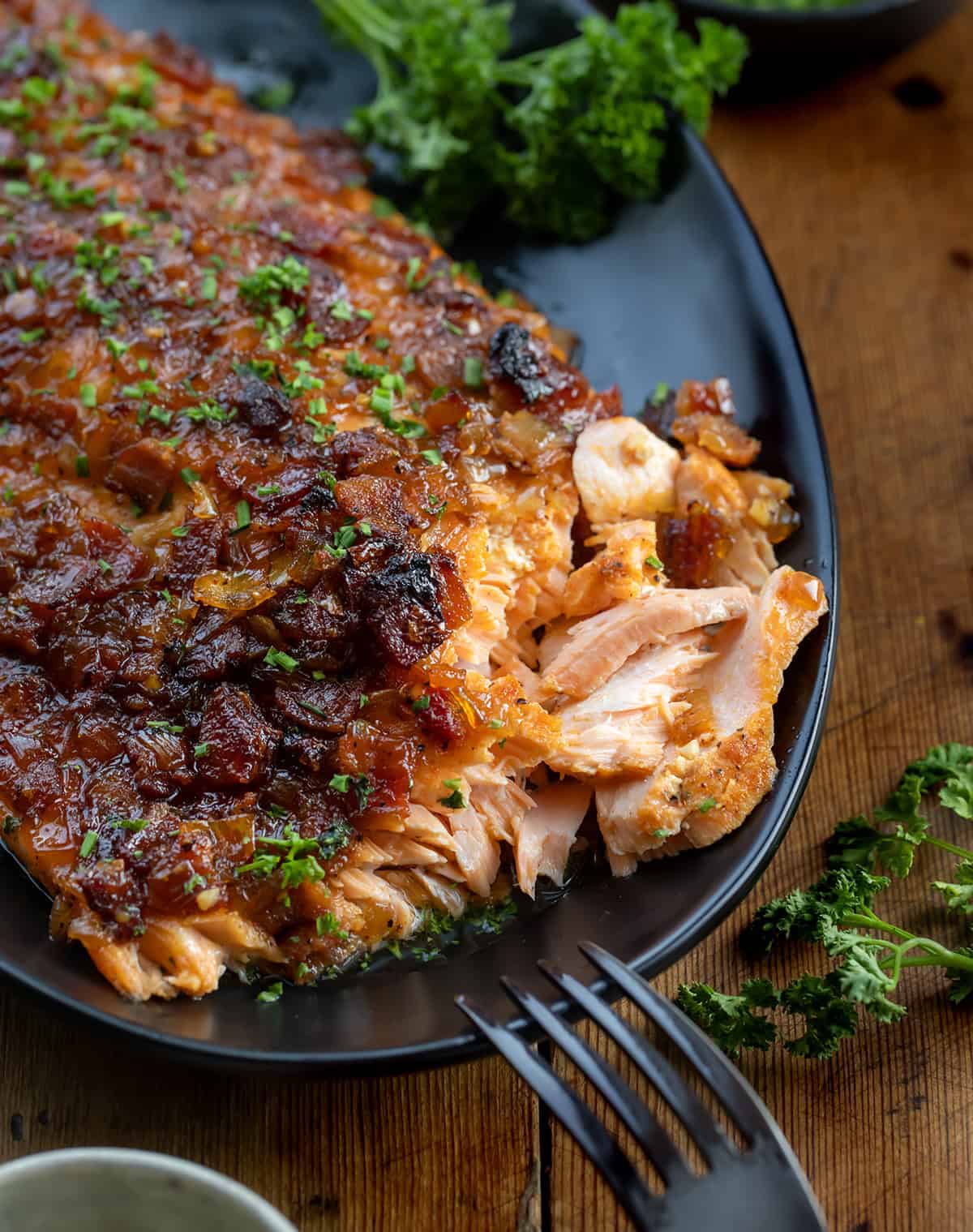 This Bacon Jam Salmon is an easy, show-stopping dinner made with my homemade onion bacon jam, which you will LOVE. The sweet, savory glaze adds rich flavor to tender, flaky salmon, perfect for weeknight dinners or special occasions! Close up of flakey Bacon Jam Salmon on a black platter.