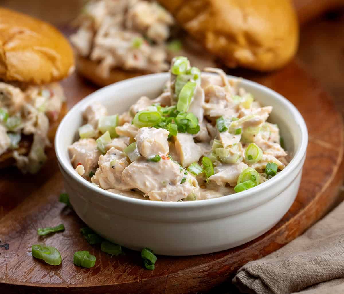 This Bang Bang Chicken Salad is creamy, slightly spicy, and ready in just minutes, perfect for a quick lunch, light dinner, or game-day spread! Small white bowl of Bang Bang Chicken Salad on a cutting board.