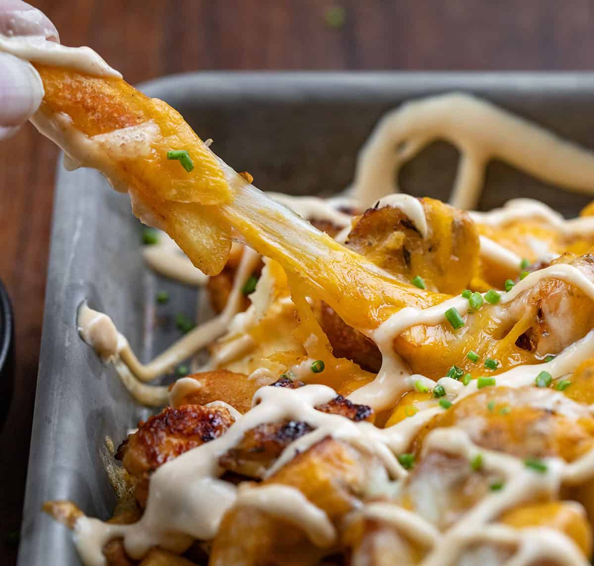 Discover the bold flavors of Cajun Chicken Loaded Fries, perfect for game day or family gatherings. Enjoy crispy, cheesy goodness! Hand picking up a Cajun Chicken Loaded Fries with stretchy cheese.