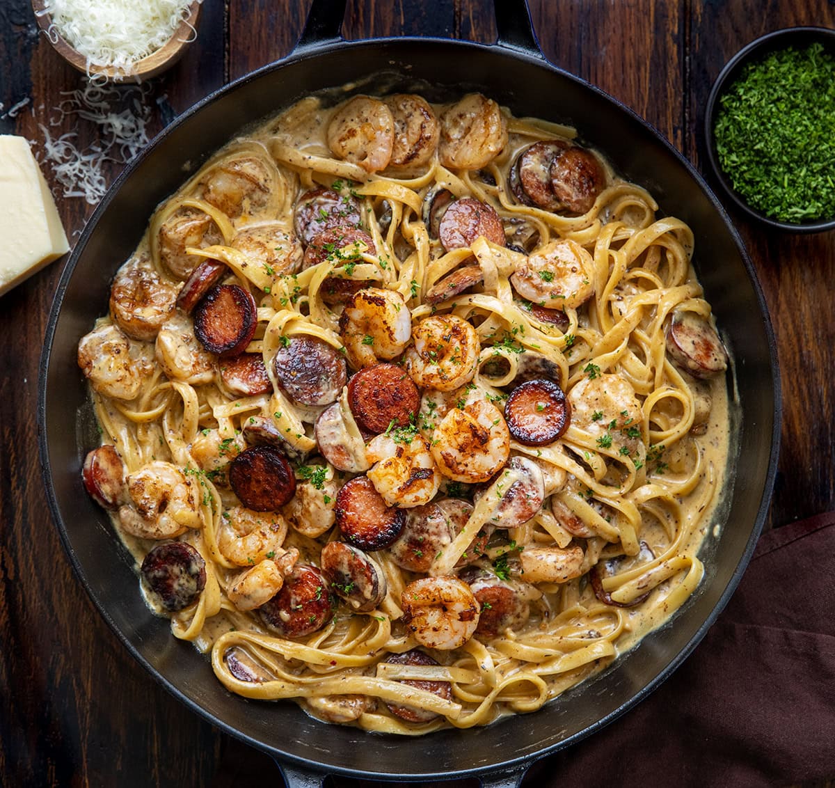 Try this Cajun Shrimp and Sausage Pasta for a spicy, creamy meal. It combines shrimp, sausage, and fettuccine in under 30 minutes! Skillet of Cajun Shrimp and Sausage Pasta on a wooden table from overhead.