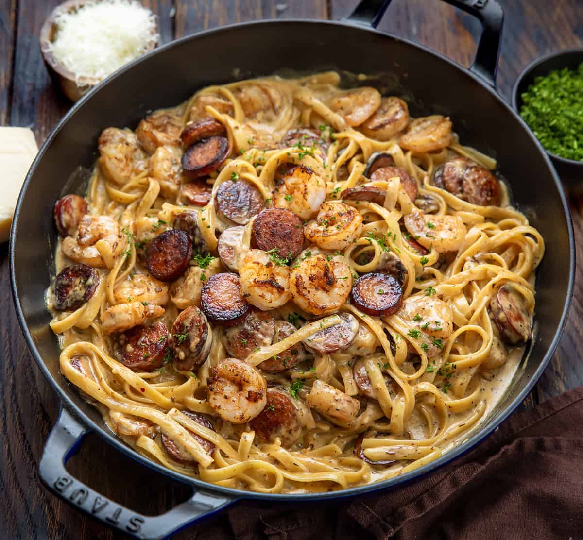Try this Cajun Shrimp and Sausage Pasta for a spicy, creamy meal. It combines shrimp, sausage, and fettuccine in under 30 minutes! Skillet of Cajun Shrimp and Sausage Pasta on a wooden table from overhead.