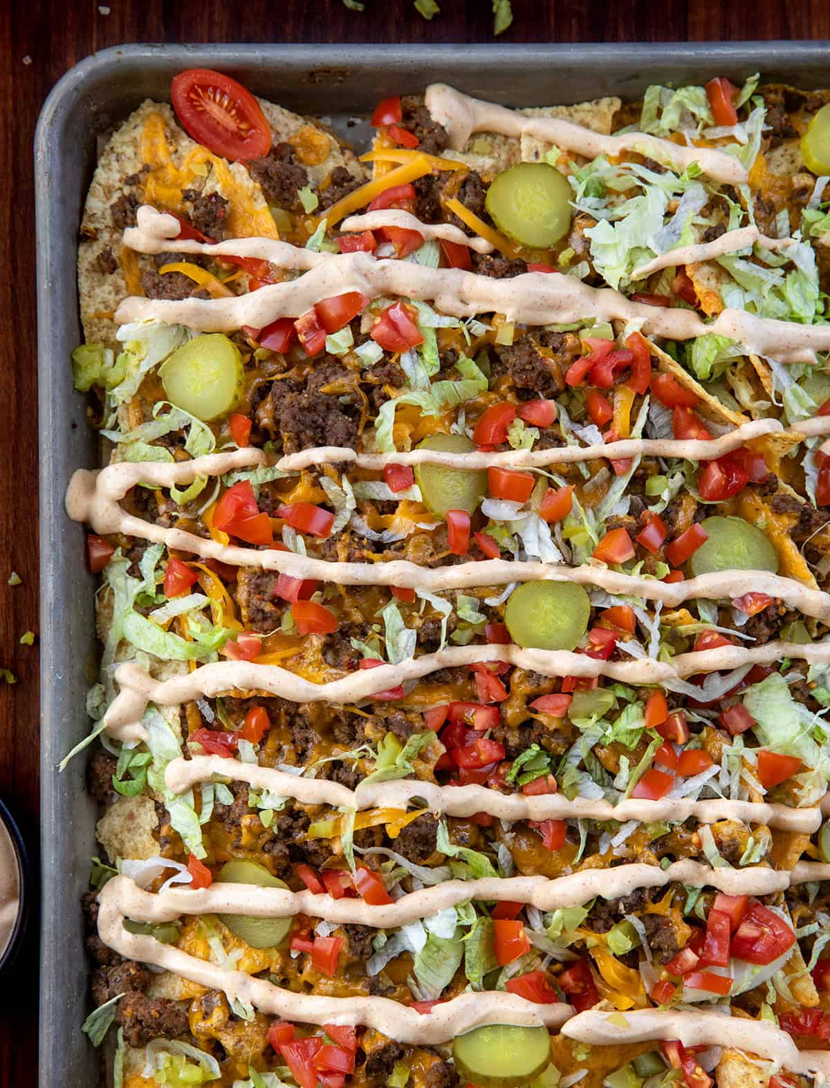 Cheeseburger Nachos are an easy, sheet-pan appetizer that’s perfect for game day or any casual gathering! Close up of Cheeseburger Nachos on a wooden table from overhead.