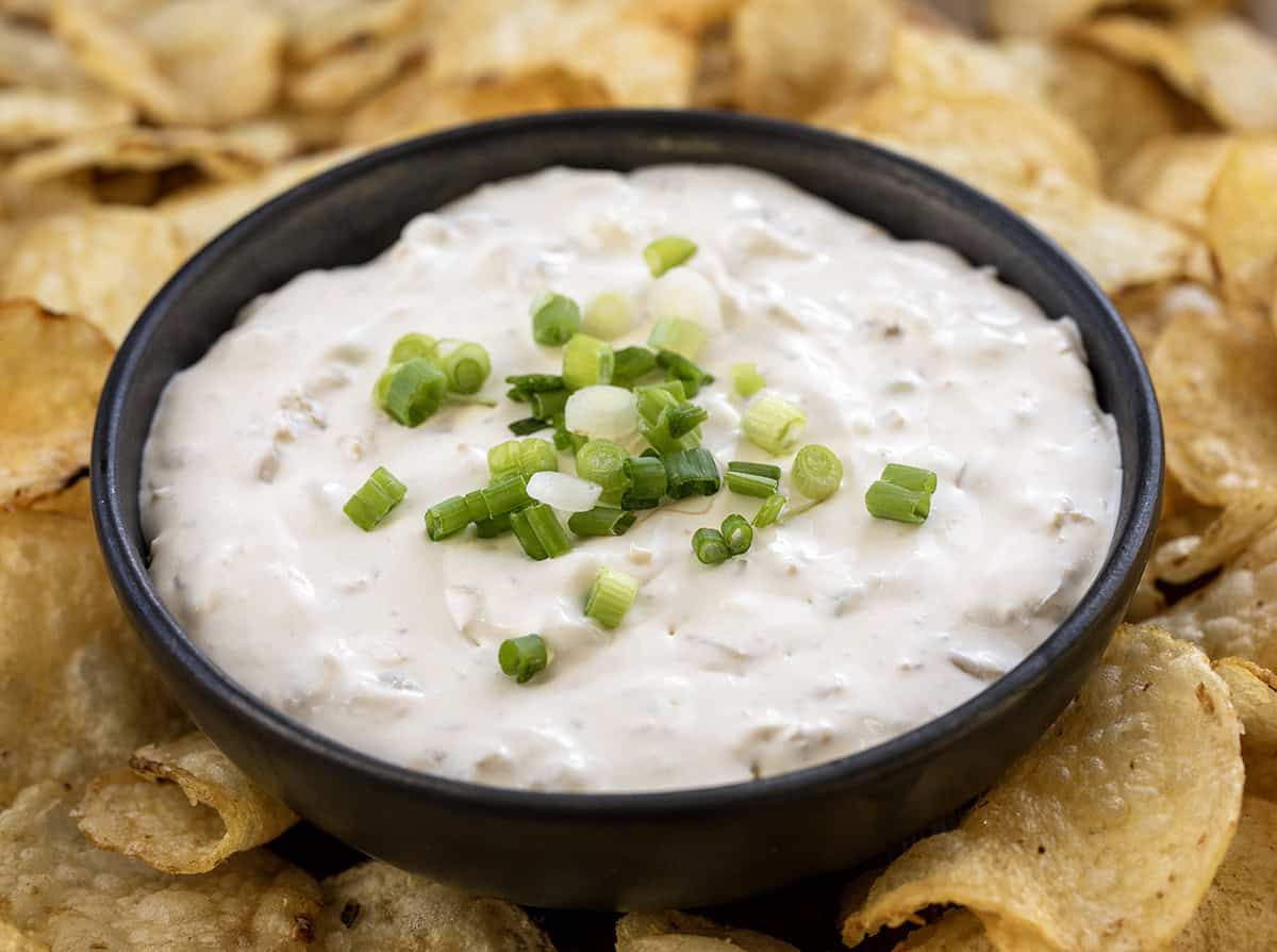 Small black bowl filled with Clam Dip surrounded by potato chips.