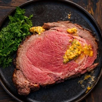 Piece of Cowboy Butter Prime Rib on a black plate on a wooden table from overhhead with some cowboy butter on the meat.