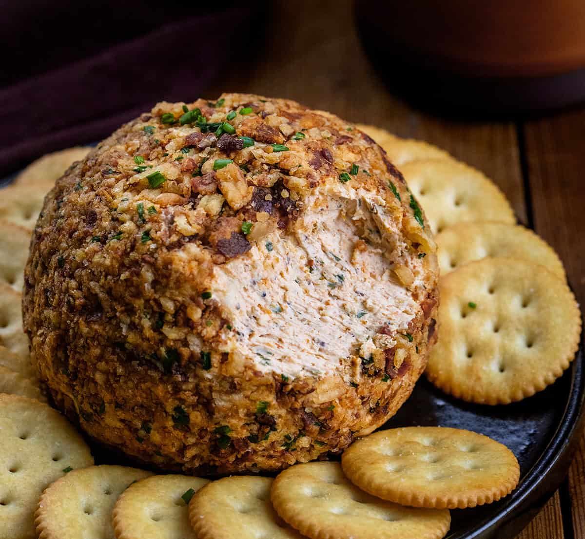 This Cowboy Cream Cheese Ball is bold, flavorful, and a guaranteed crowd-pleaser. It’s based on my classic Cowboy Cream Cheese, with pepperjack cheese, spices, and a hint of heat, topped with crispy bacon, and crunchy French’s onions! Cowboy Cream Cheese Ball with some removed showing the inside and surrounded by crackers.