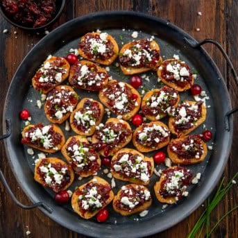 Platter of Cranberry Bacon Jam and Feta Crostini on a wooden table from overhead.