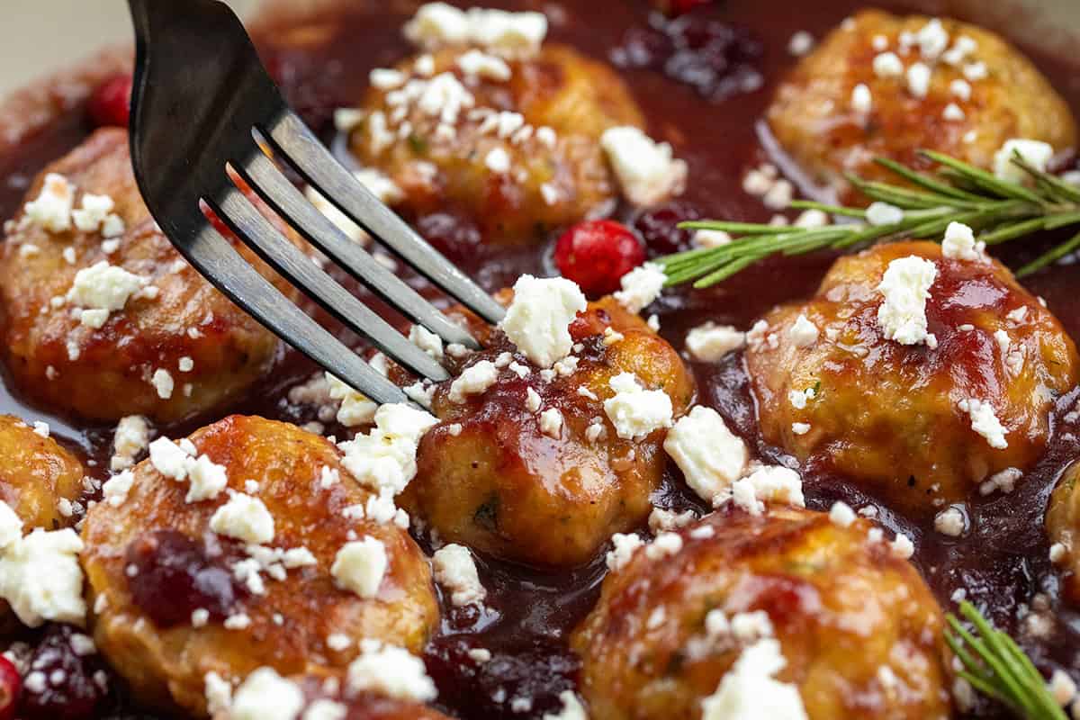 These Cranberry Feta Chicken Meatballs are sweet, savory, and irresistibly festive. Serve them as an appetizer or over rice or pasta for a comforting seasonal meal! Fork picking up a Cranberry Feta Chicken Meatball.