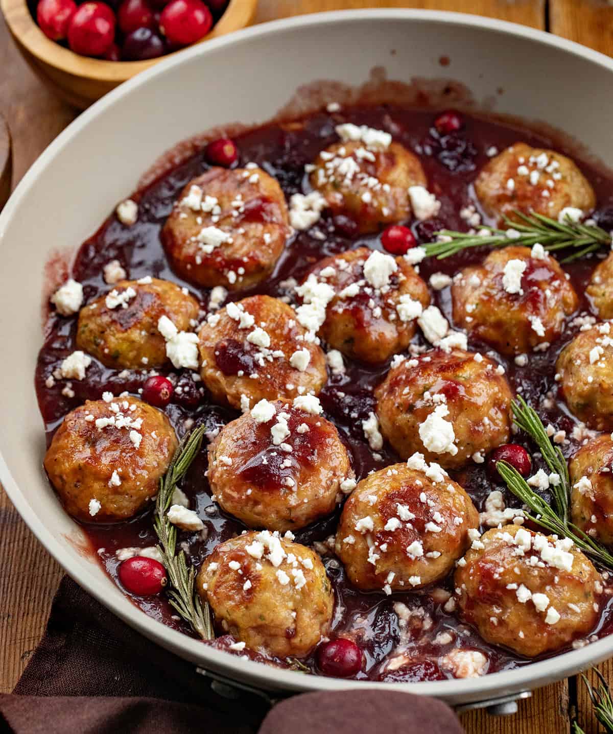 These Cranberry Feta Chicken Meatballs are sweet, savory, and irresistibly festive. Serve them as an appetizer or over rice or pasta for a comforting seasonal meal! Cranberry Feta Chicken Meatballs in a skillet on a wooden table.