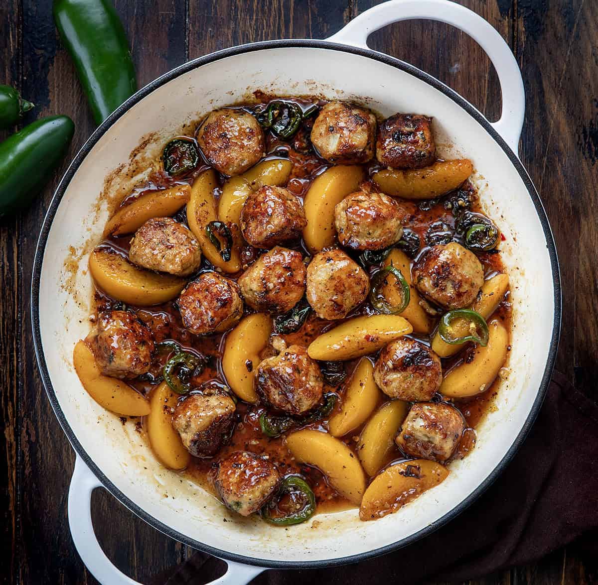 White Skillet of Jalapeño Peach Chicken Meatballs on a wooden table from overhead.