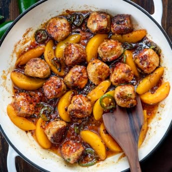 White skillet of Jalapeño Peach Chicken Meatballs on a wooden table from overhead with a spoon in it.