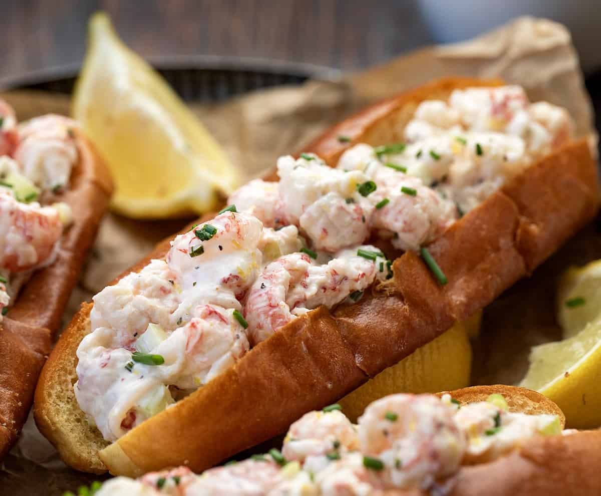These Langostino Lobster Rolls are my quick, easy take on a classic New England favorite. Sweet, tender langostino takes the place of lobster tails, tossed in a bright, lemony mayo with celery and chives, then served in buttery toasted brioche buns! Close up of Langostino Lobster Rolls on a tray with lemon.