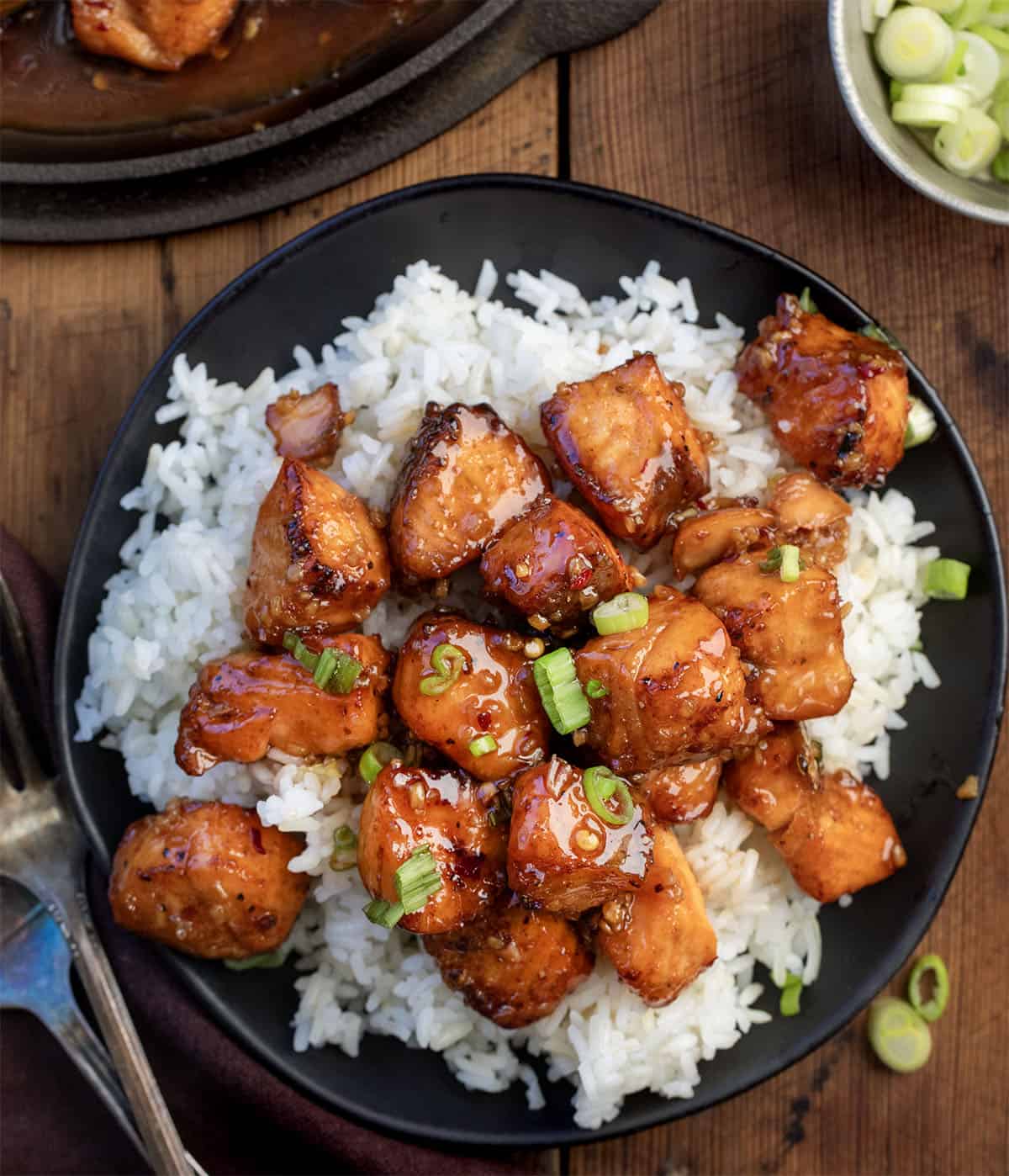 These Maple Glazed Salmon Bites are crispy on the outside, tender in the center, and coated in a sweet-and-savory maple glaze that clings to every bite. Made quickly in the air fryer or oven! Maple Glazed Salmon Bites on white rice on a black plate from overhead.