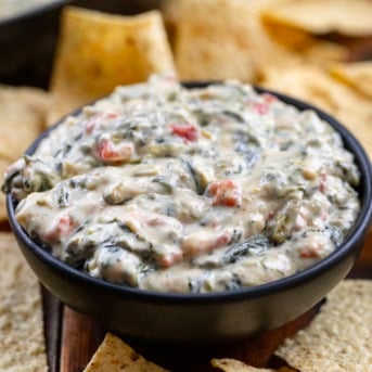 Small black bowl of Spinach Queso Dip surrounded by tortilla chips.