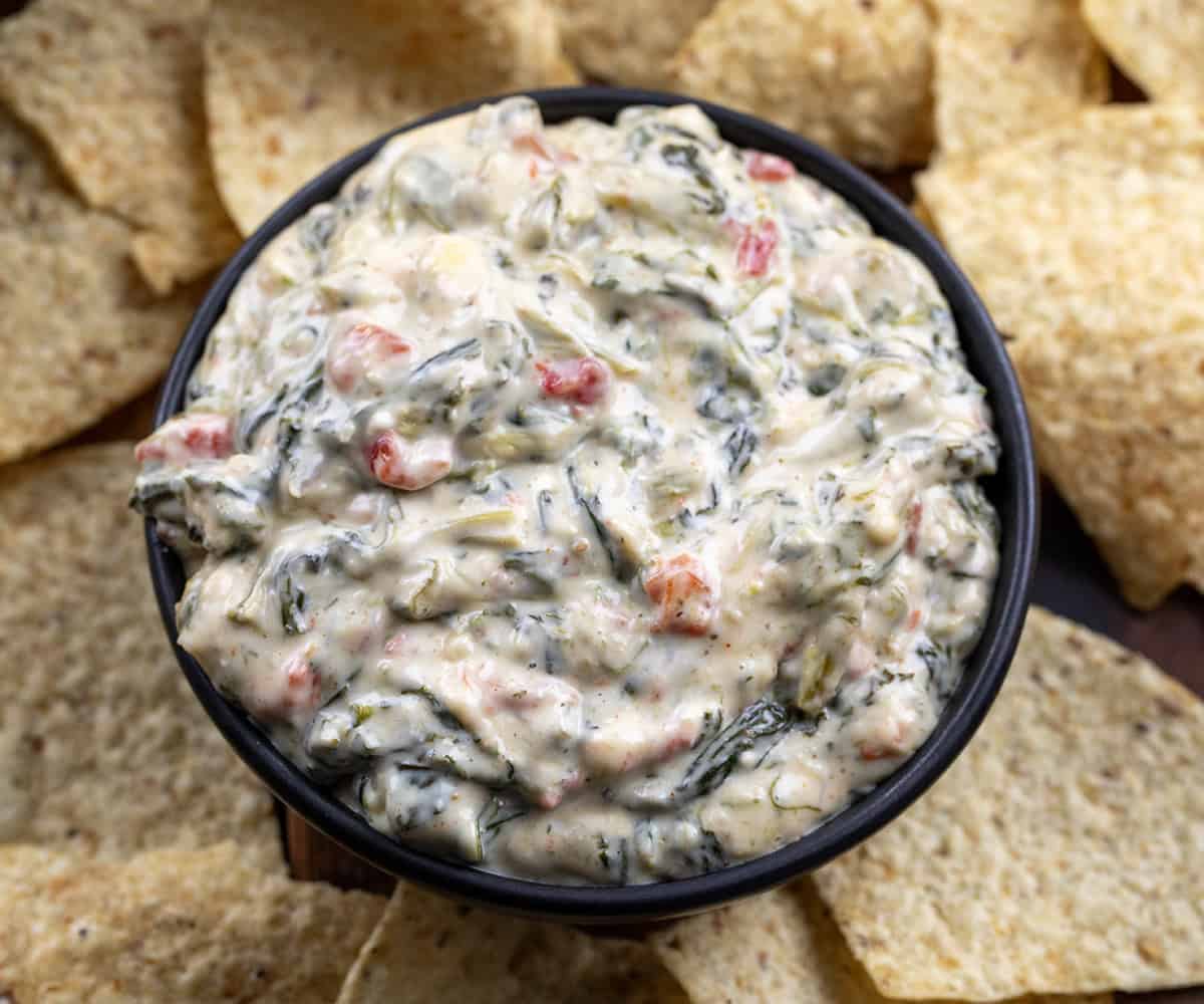 Small black bowl of Spinach Queso Dip surrounded by tortilla chips.