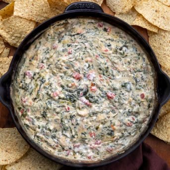 Skillet of Spinach Queso Dip on a wooden table with tortilla chips around.