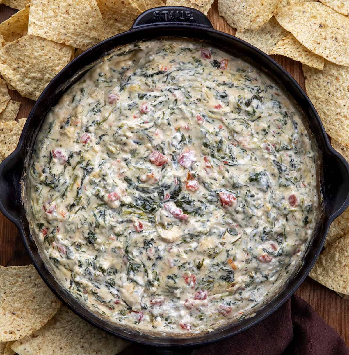 Skillet of Spinach Queso Dip on a wooden table with tortilla chips around.