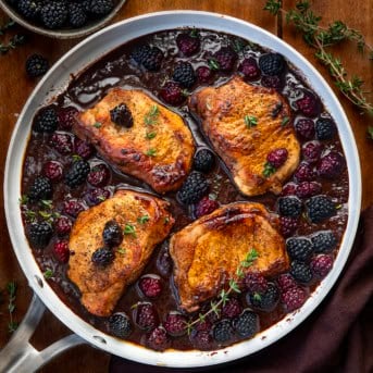 Pan of Bourbon Blackberry Pork Chops on a wooden table with fresh blackberries from overhead.