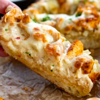 Hand picking up a slice of cut into Chicken Alfredo Garlic Bread.