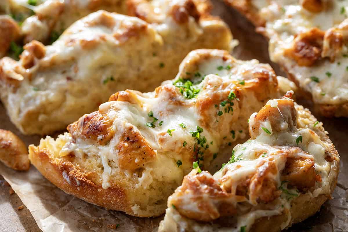 This Chicken Alfredo Garlic Bread combines toasted garlic bread with creamy Alfredo sauce and seasoned chicken for an easy, crowd-pleasing meal or appetizer. It’s simple to make, incredibly filling, and always the first thing gone! Close up of cheesy gooey Chicken Alfredo Garlic Bread.