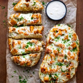 Chicken Alfredo Garlic Bread on a wooden table with one half cut into slices and the other half uncut.