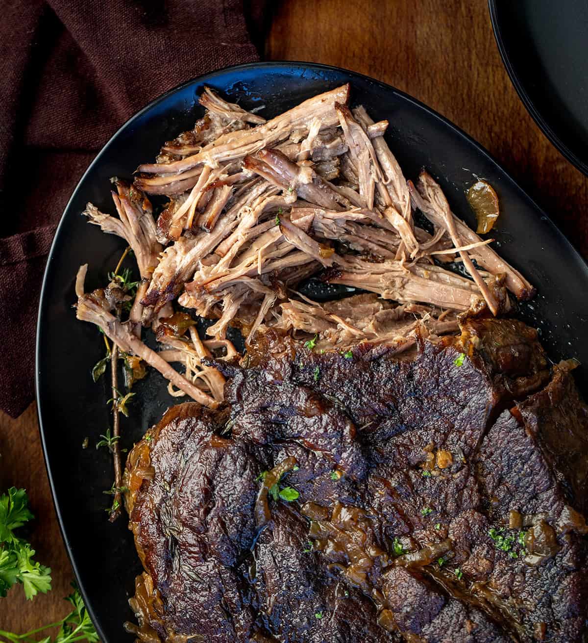 There’s nothing quite like a slow-cooked, fork-tender chuck roast fresh from the oven. This classic oven-braised roast develops rich, savory flavors with minimal effort, perfect for a cozy weeknight dinner or a weekend family meal! Oven Chuck Roast with some of it shredded on a black platter on a wooden table.