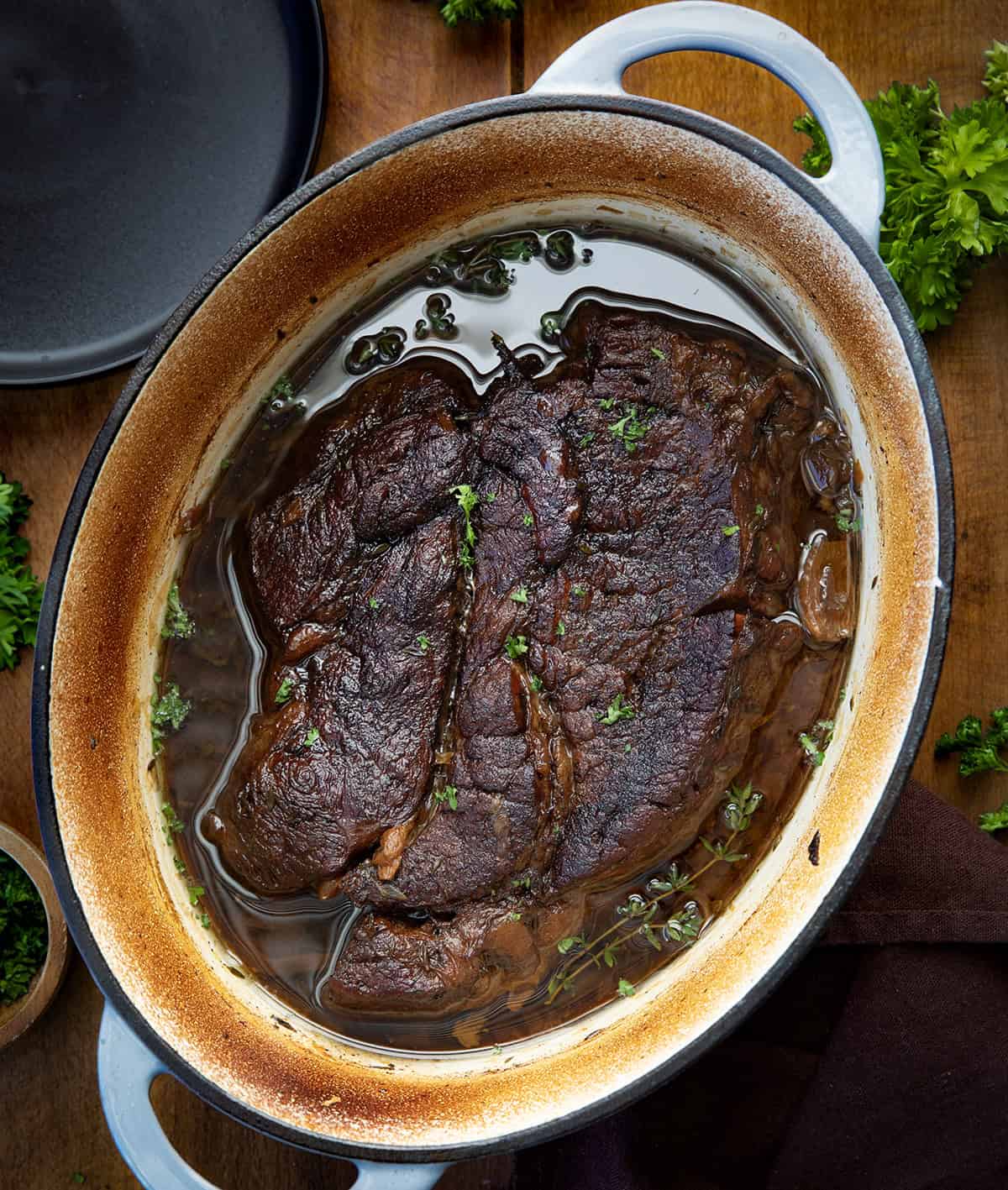 There’s nothing quite like a slow-cooked, fork-tender chuck roast fresh from the oven. This classic oven-braised roast develops rich, savory flavors with minimal effort, perfect for a cozy weeknight dinner or a weekend family meal! Oven Chuck Roast in a pot on a wooden table from overhead.