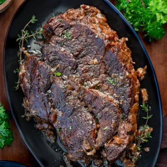 Whole Oven Chuck Roast on a black platter on a wooden table.