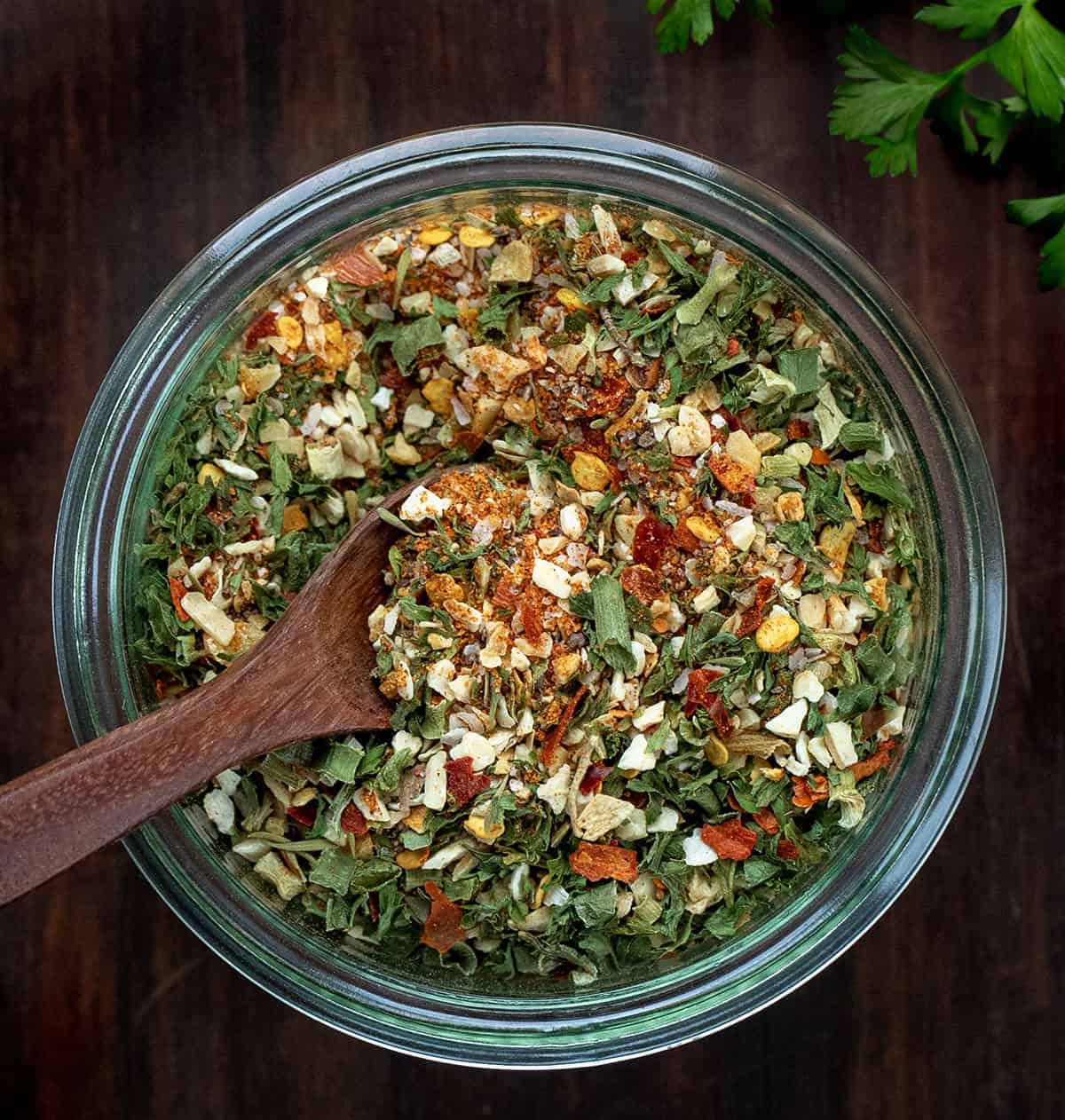 This Cowboy Butter Seasoning is a bold, savory, and slightly spicy blend of herbs and spices that transforms butter, mayonnaise, or cream cheese into flavorful spreads! Jar of Cowboy Butter Seasoning on a wooden table with a mini wooden spoon in the jar.