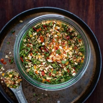 Jar of Cowboy Butter Seasoning on a black plate with a metal teaspoon next to the jar.