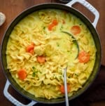 Pot of Ginger Turmeric Chicken Soup with a ladle in it on a wooden table.